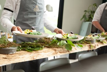 Plankebræt med blade og tallerkener bliver serveret af tjener til Local Cooking 2019