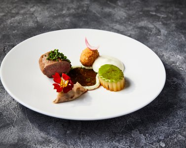 Hvid tallerken på grå bordplade med kød, kartoffelkrokette, en lille tærte, skum, spiselige blomster og en brun sauce, lavet af Magnus Carlsen til Kartoffelrprisen 2020 